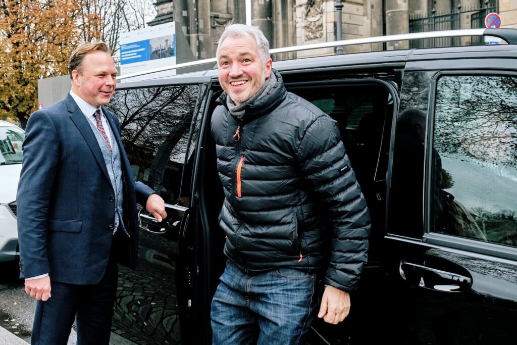 Private driver welcoming a traveler to a comfortable Berlin shore excursion vehicle.
