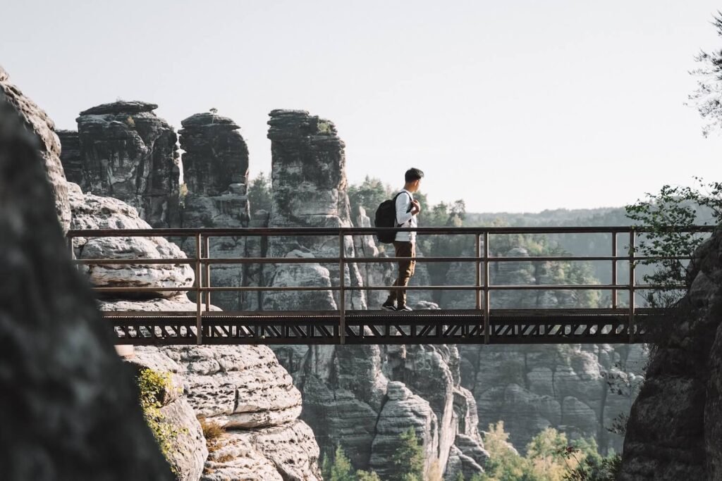 Hiker crossing a bridge between sandstone cliffs in Saxon Switzerland