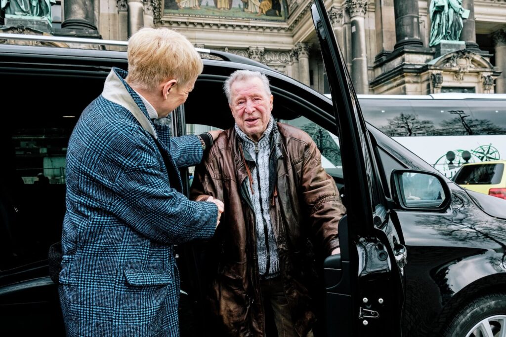 Guide assisting an older traveler from a private vehicle by Berlin Cathedral on a family history tour